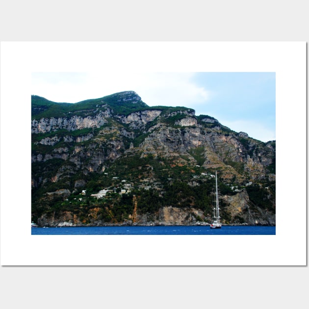View in Amalfi coast at a huge mountain with rocky parts, greenery and buildings with a white boat underneath Wall Art by KristinaDrozd